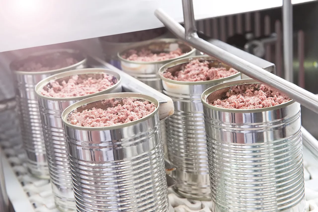 Förderanlage mit metallischen Körben voller Fleischstückchen, transportiert innerhalb der Produktionshalle.