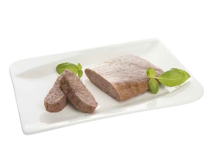 Rechteckiger Fleischpastetenblock mit zwei Scheiben und Basilikumblättern auf weißem Teller.
